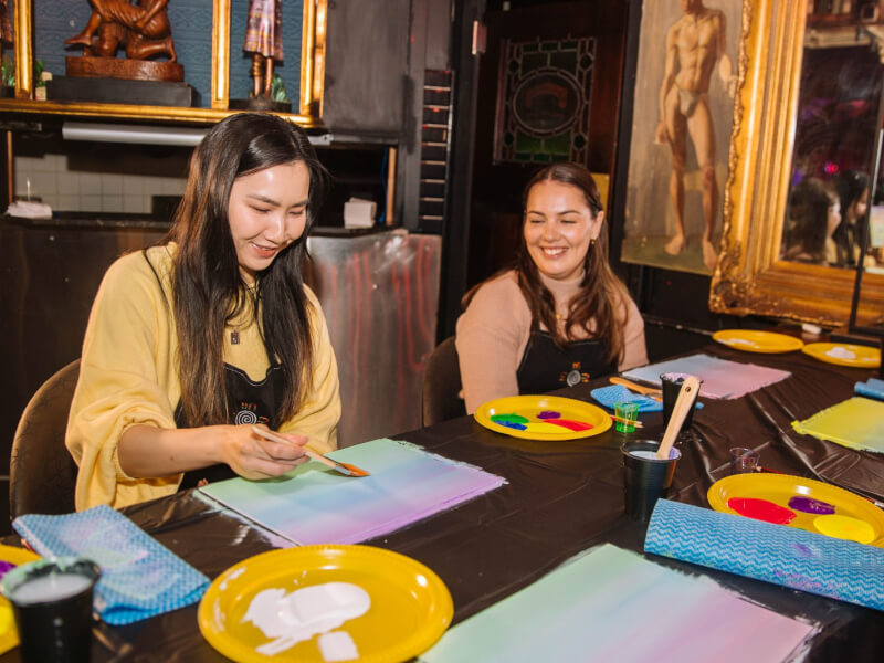 Two women smiling as they paint together on a date